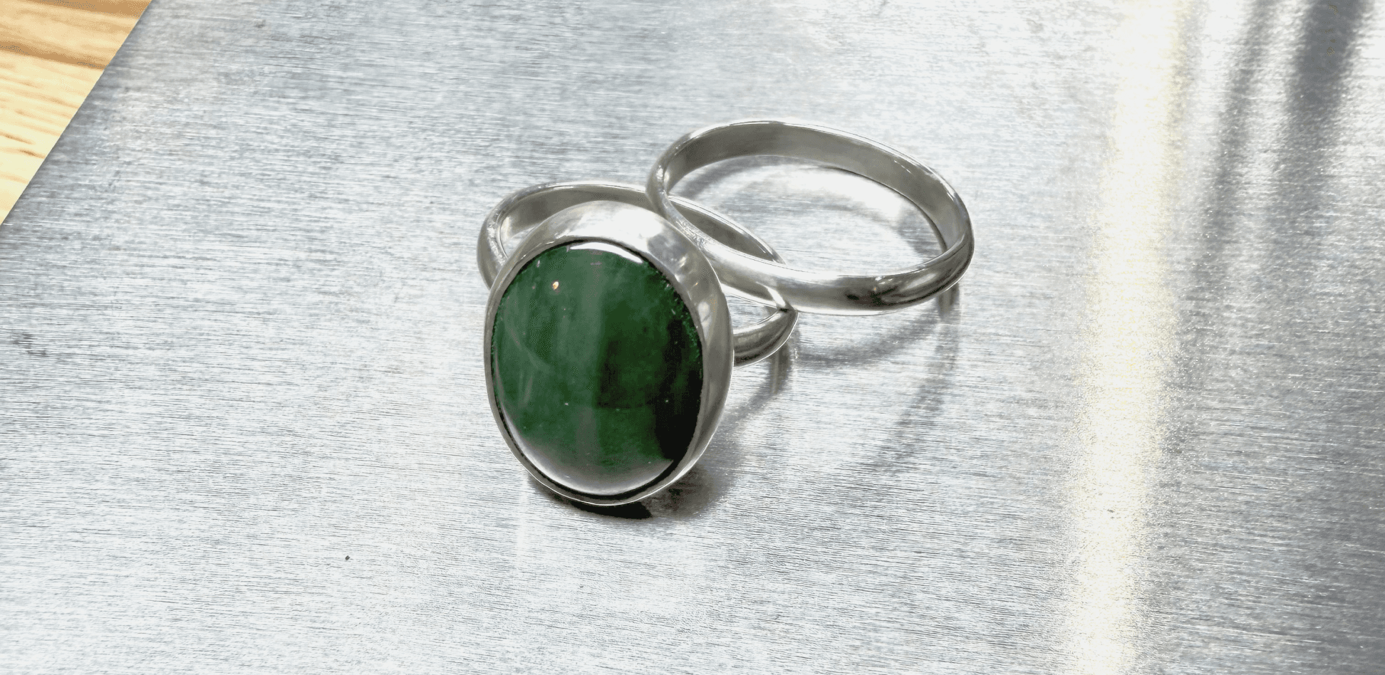 A finished sterling silver ring set with a cabochon-cut green stone, resting on a workbench.