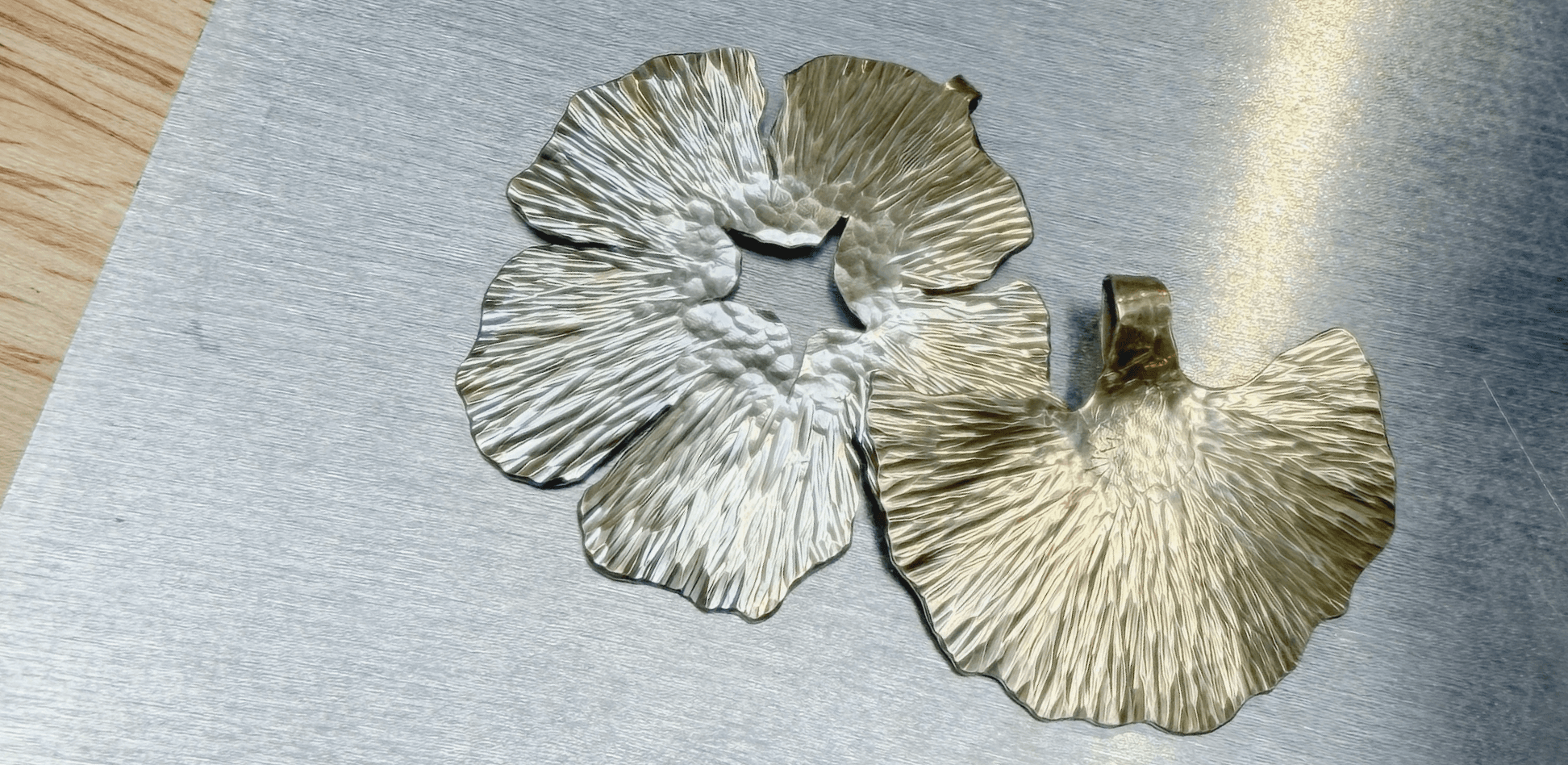 Hammered brass leaf-form earrings mid-process on a metalsmithing bench.
